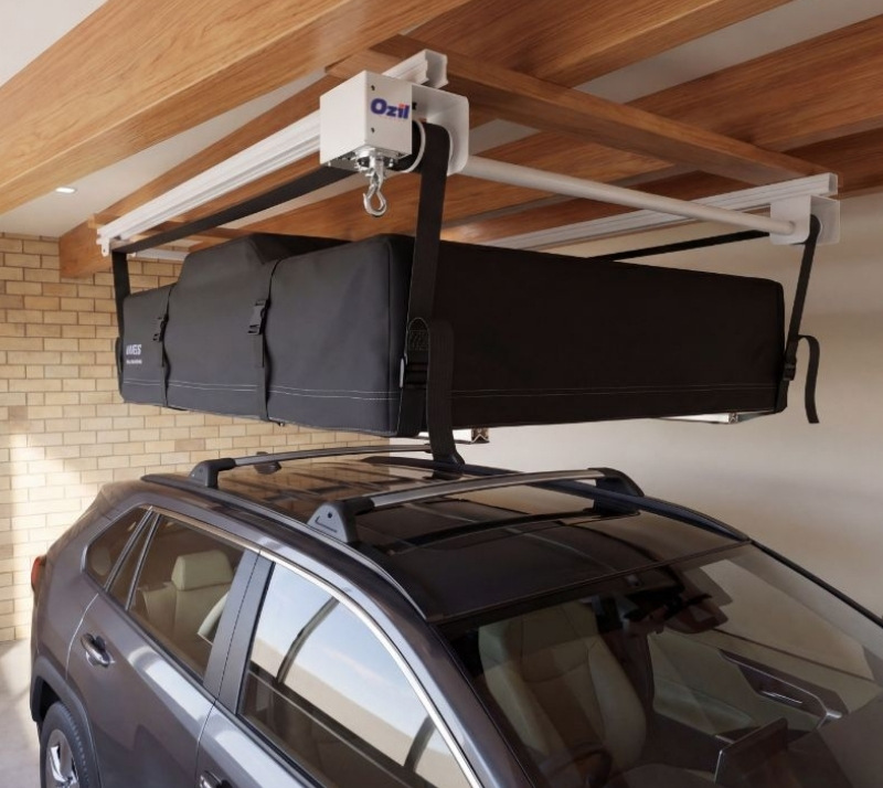 Vehicle with a black roof cargo bag mounted on a ceiling Hoist rack above in a garage with wooden beams.